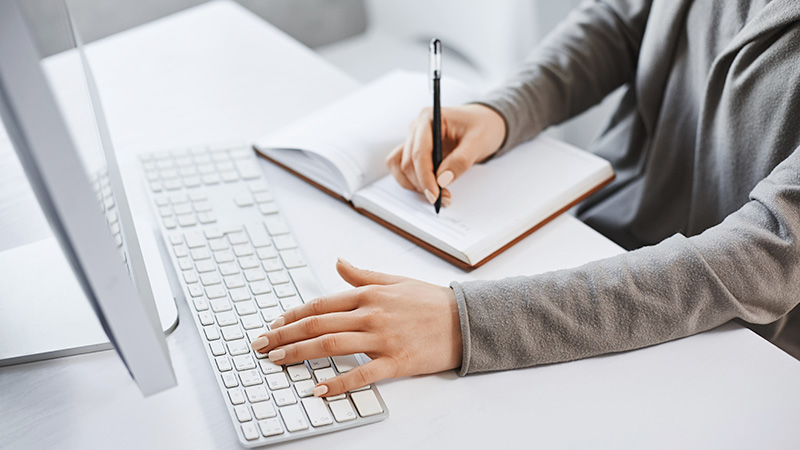 Preparing-an-effective-procurement-brief Person looking at computer screen and writing in notebook