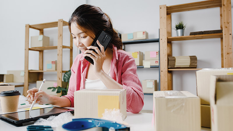 Grow-Your-Business Woman of phone with package boxes and packing tape around her